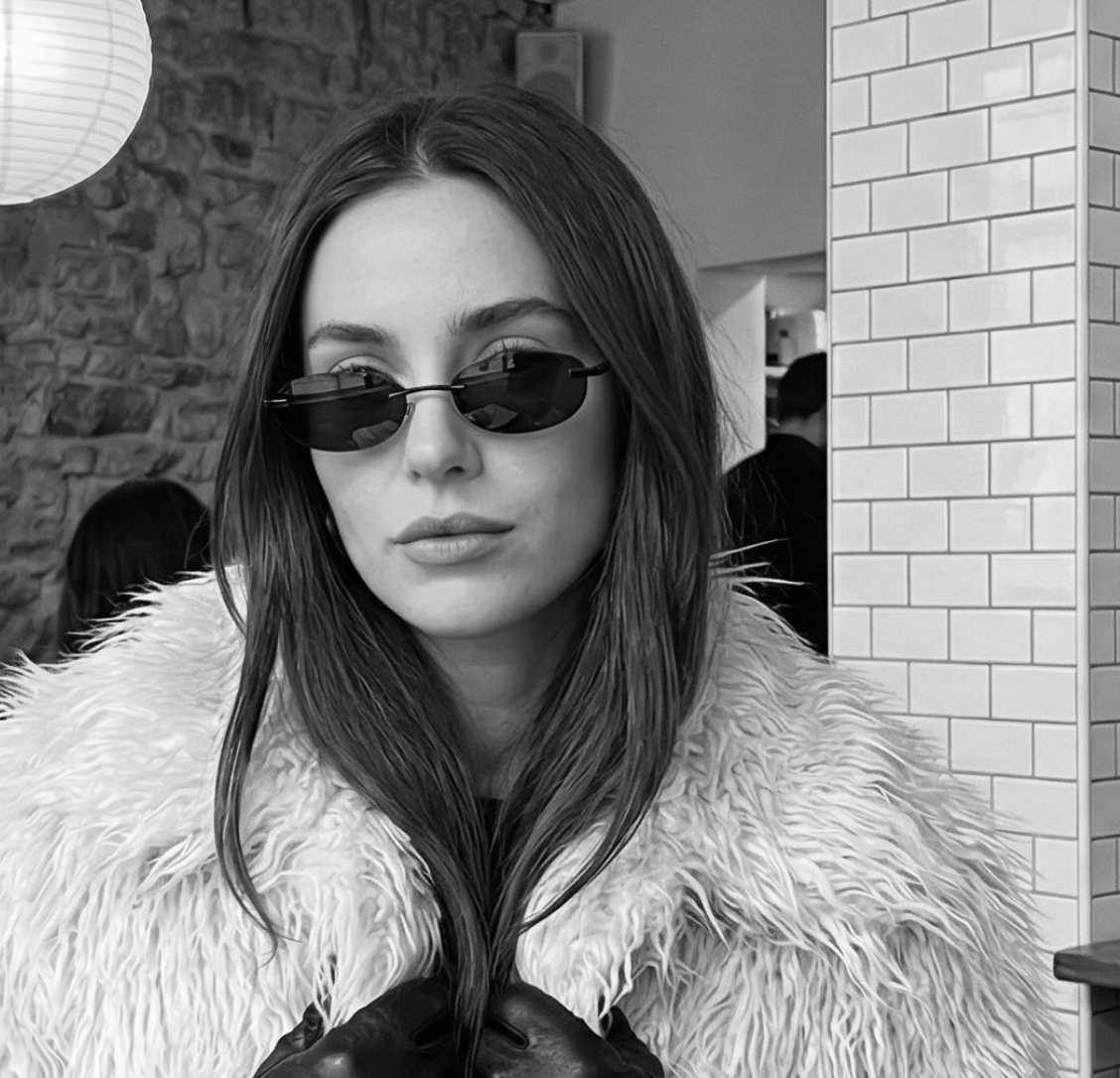 Person wearing sunglasses and a fluffy coat in a black and white setting