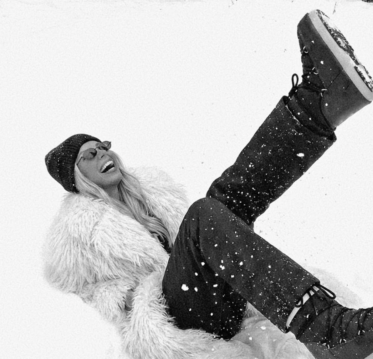 Person lying on the snow wearing a fur coat and boots