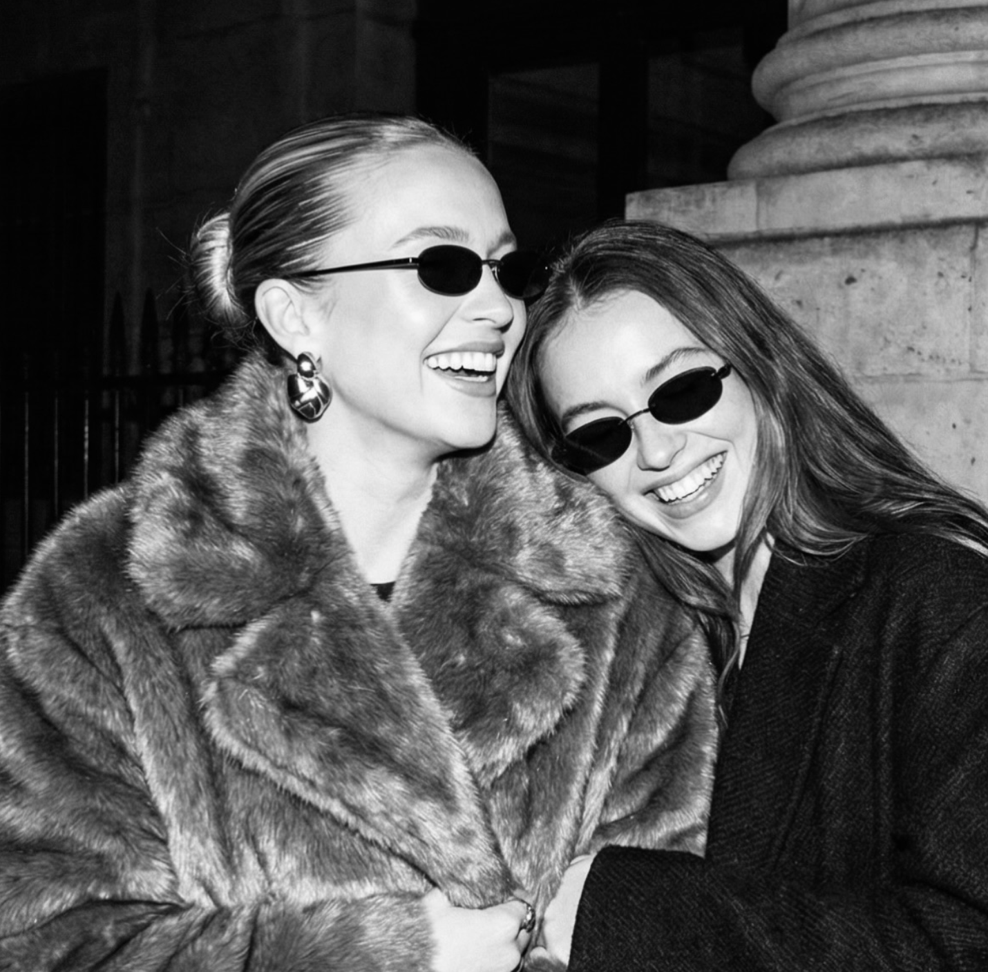 Two women wearing sunglasses and smiling outdoors.