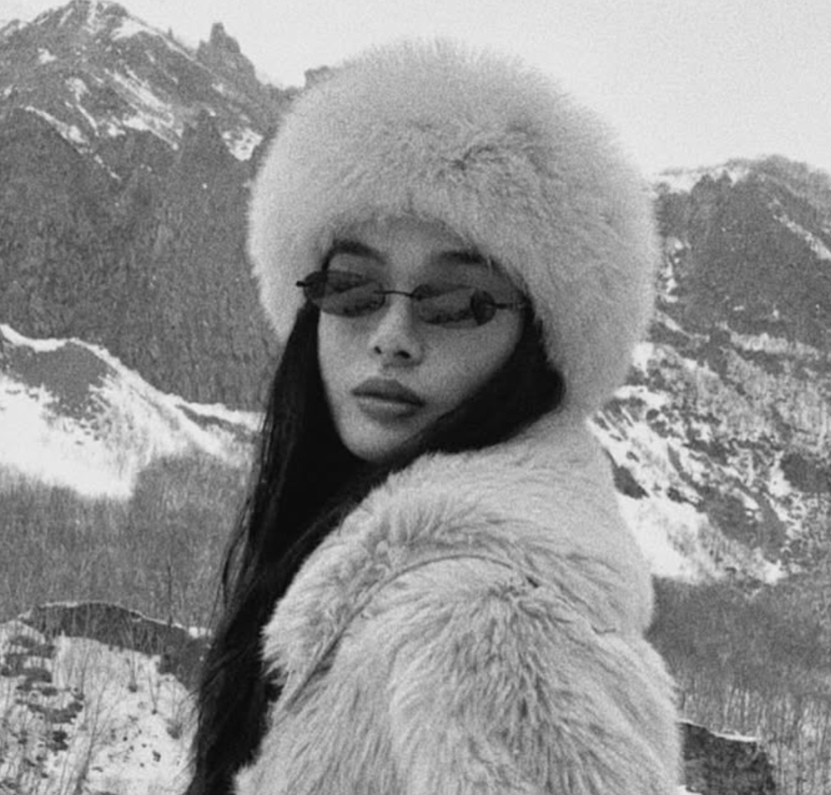 Person wearing a fur coat and hat with a snowy mountain background